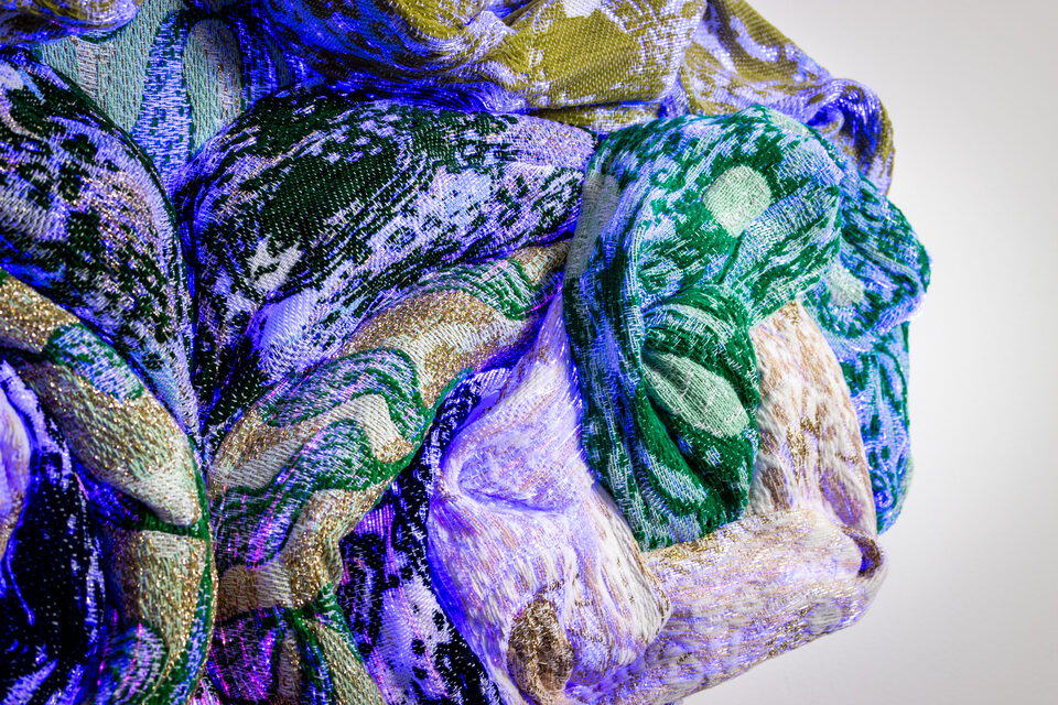 Close-up of Emerald's woven textile, intricate green and golden-yellow threads.
