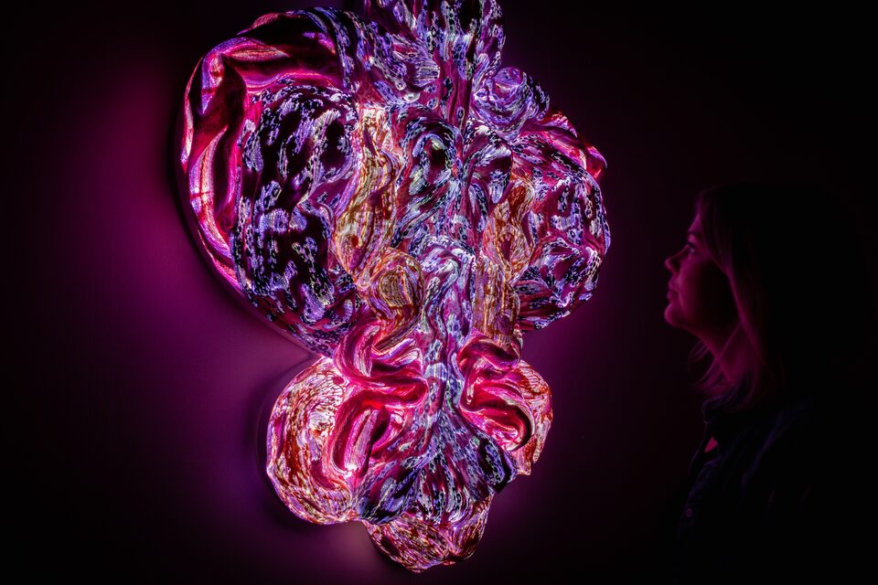 Visitor gazing at a large glowing textile sculpture in purple and magenta at ANDETAG Stockholm