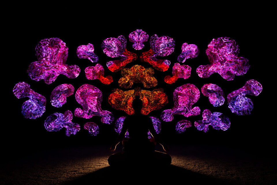 Person meditating cross-legged beneath a symmetrical spread of glowing textile sculptures at ANDETAG Stockholm