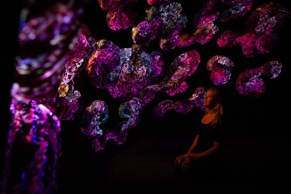 Visitor sitting on the floor looking up at a cluster of glowing pink textile sculptures at ANDETAG Stockholm