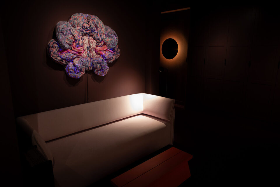 Quiet lounge with a white sofa beneath a backlit textile sculpture at ANDETAG Stockholm