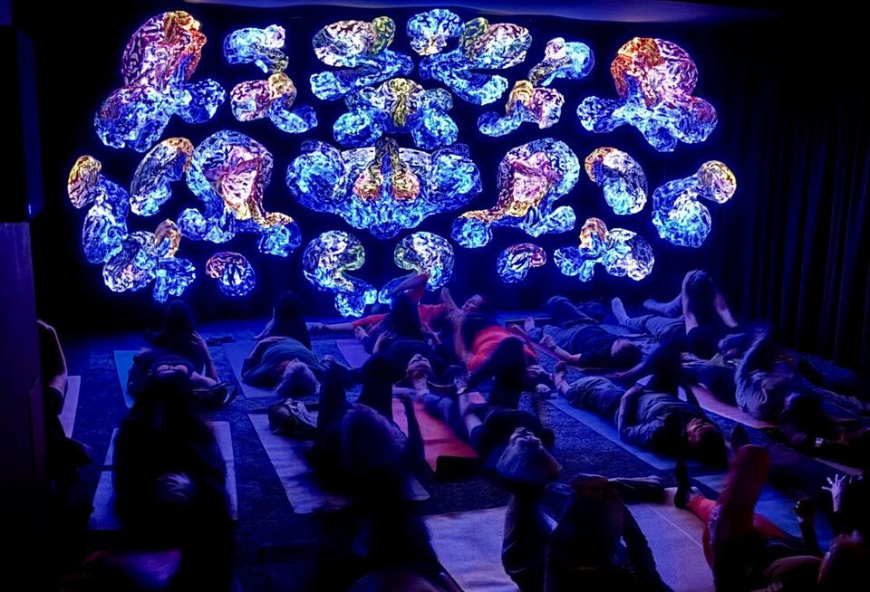 Group of participants lying on yoga mats during Art Yoga at ANDETAG, facing a wall of glowing light sculptures at ANDETAG museum