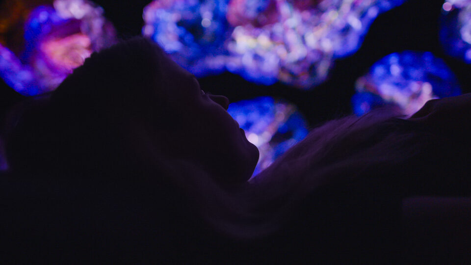 Person in silhouette lying back and gazing up at glowing light sculptures at ANDETAG museum