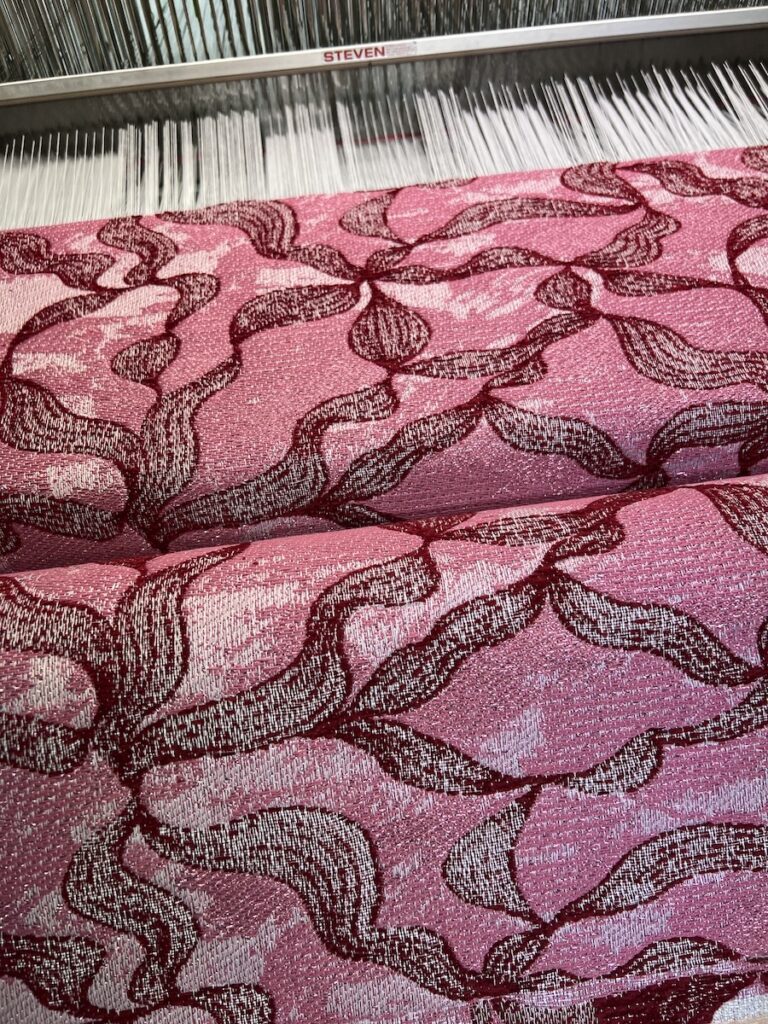 Close-up of pink and burgundy optical fibre textile on the loom with a winding jacquard pattern
