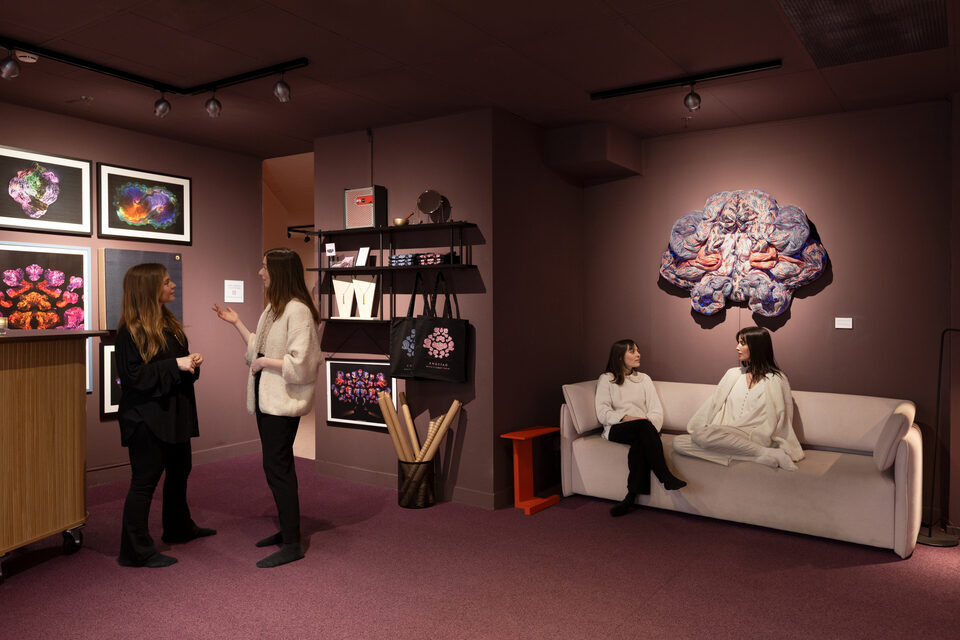 The museum lobby with framed textile works, a sofa with visitors, and a large wall sculpture at ANDETAG.