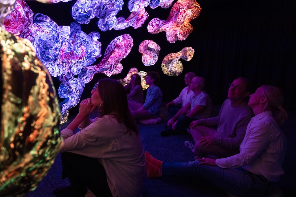 A group of visitors leaning back towards luminous textile art in purple and blue tones.