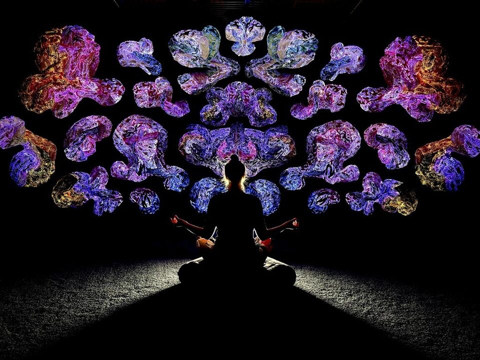 Siluett av person i meditation framför symmetriska, lysande textilformer i lila, rosa och guld.